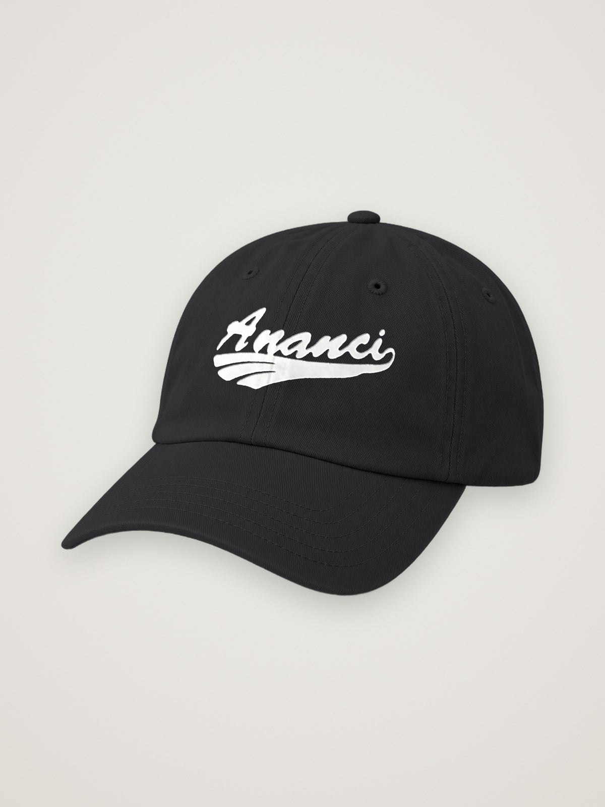 Black ANANCI script dad hat with the wordmark embroidered in white, on a warm stone background