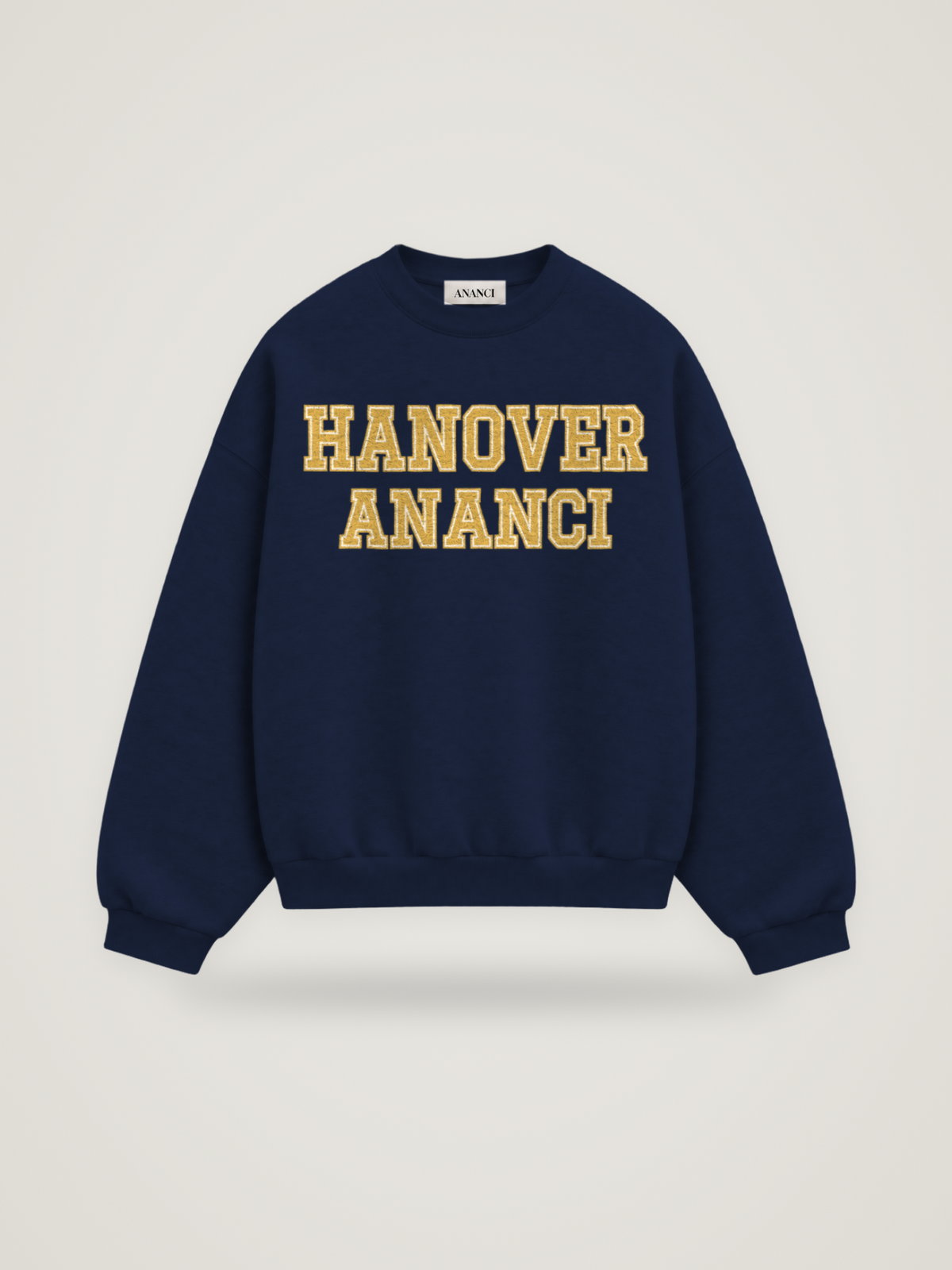 Front of the midnight ANANCI Where Yuh From? Hanover crewneck with straight two-tone varsity lettering, gold with a cream inline, reading HANOVER over ANANCI