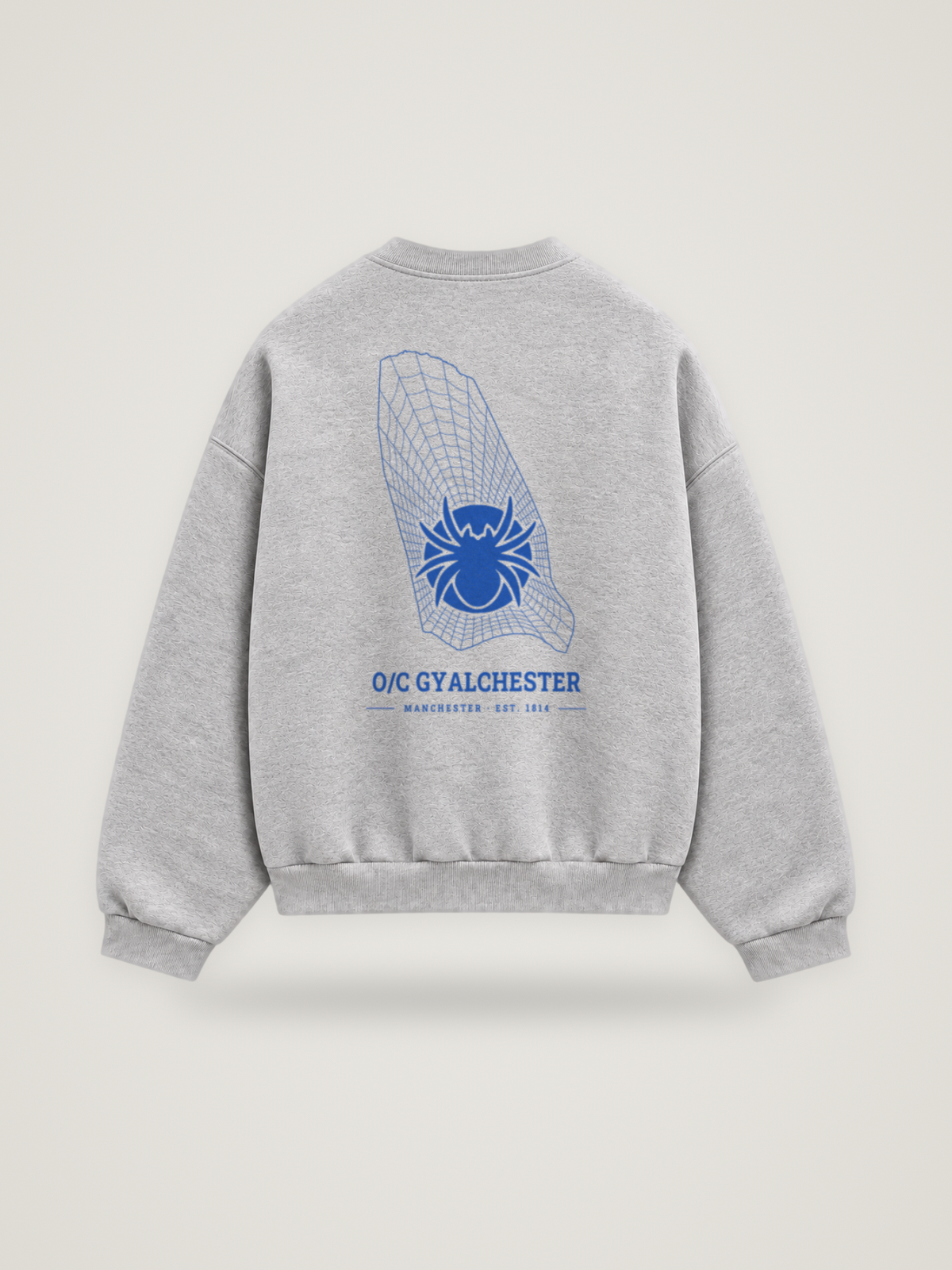 Back of the heather grey ANANCI Where Yuh From? Manchester crewneck with the Manchester map, web and spider in cobalt ink, “O/C GYALCHESTER” and MANCHESTER · EST. 1814