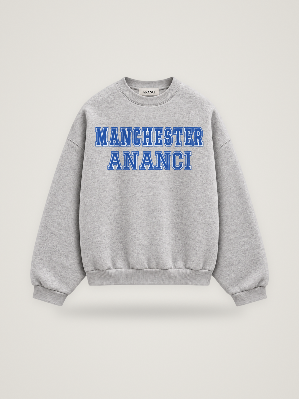 Front of the heather grey ANANCI Where Yuh From? Manchester crewneck with straight two-tone varsity lettering, cobalt with a white inline, reading MANCHESTER over ANANCI