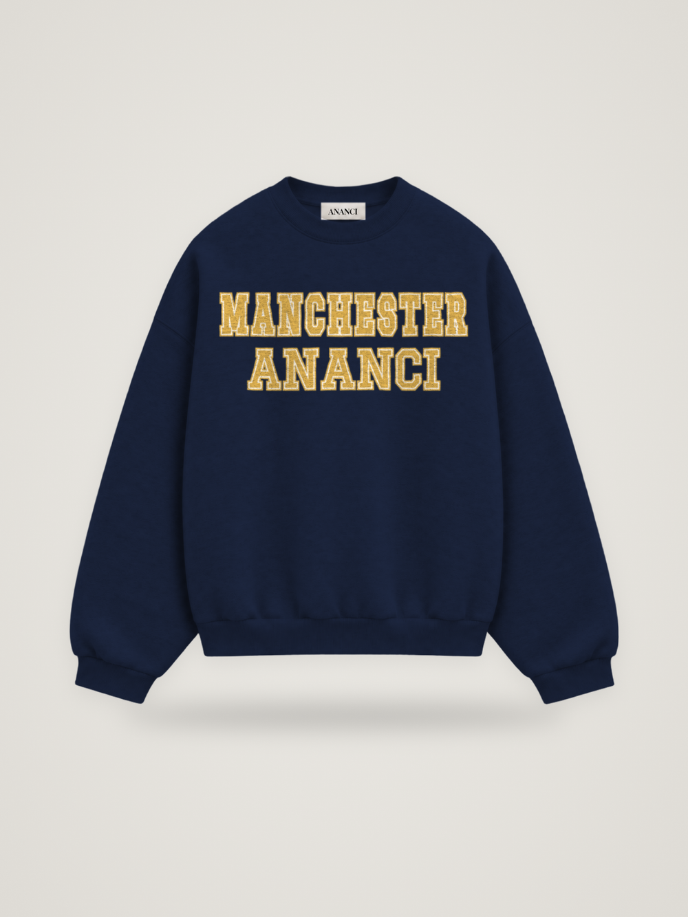 Front of the midnight ANANCI Where Yuh From? Manchester crewneck with straight two-tone varsity lettering, gold with a cream inline, reading MANCHESTER over ANANCI