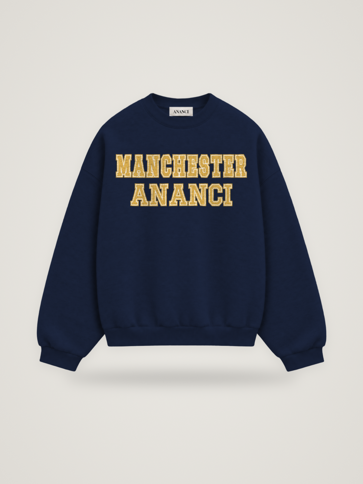 Front of the midnight ANANCI Where Yuh From? Manchester crewneck with straight two-tone varsity lettering, gold with a cream inline, reading MANCHESTER over ANANCI
