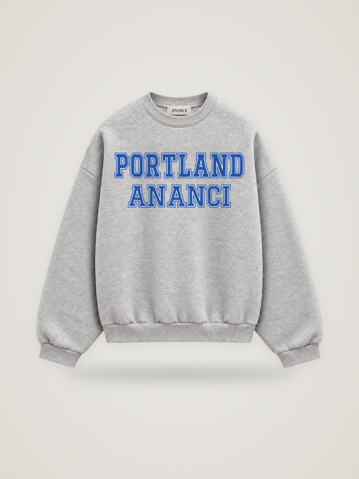 Front of the heather grey ANANCI Where Yuh From? Portland crewneck with straight two-tone varsity lettering, cobalt with a white inline, reading PORTLAND over ANANCI