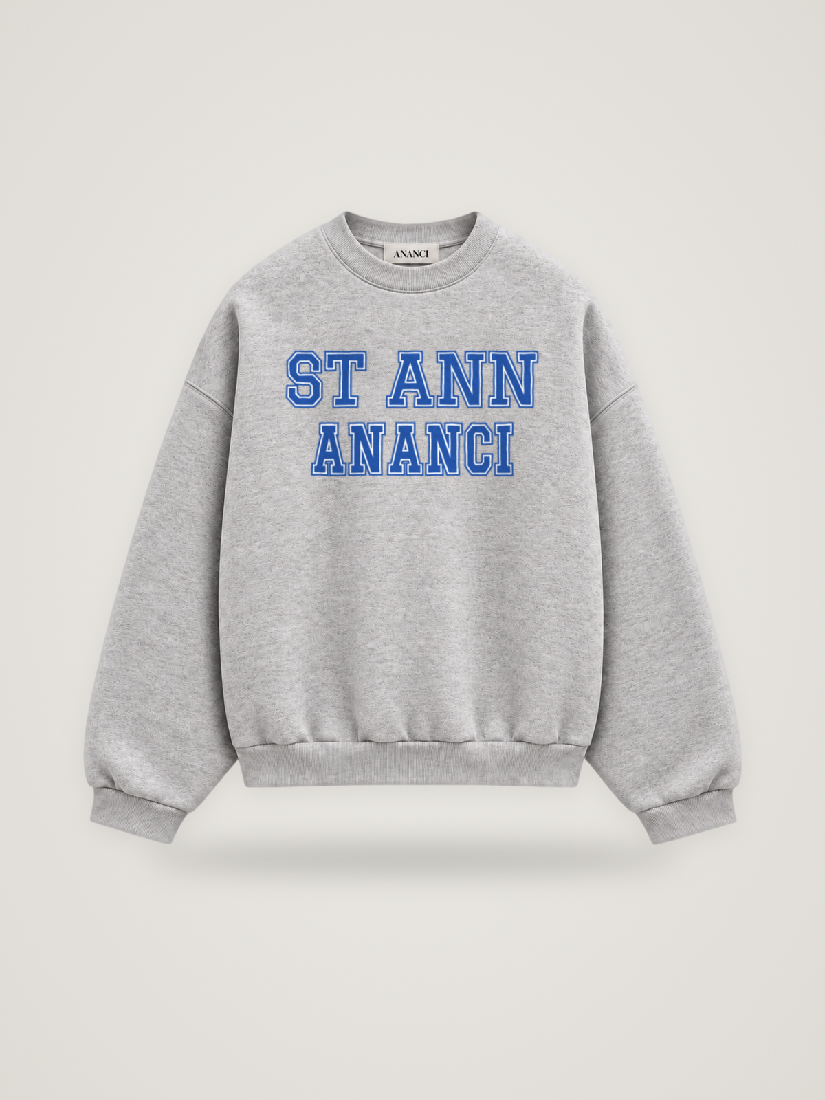 Front of the heather grey ANANCI Where Yuh From? St Ann crewneck with straight two-tone varsity lettering, cobalt with a white inline, reading ST ANN over ANANCI