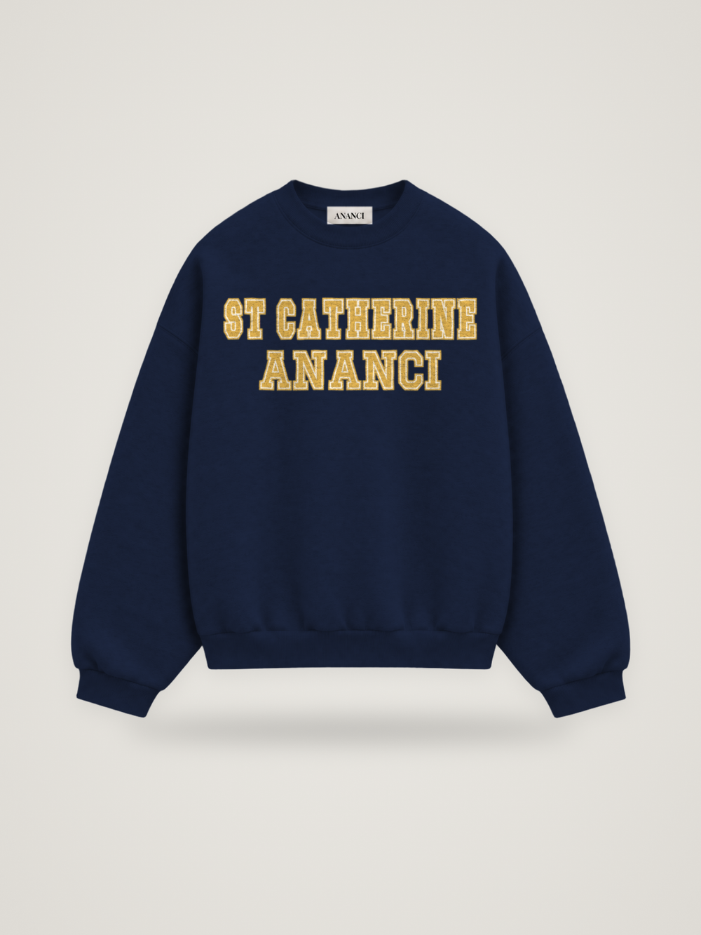 Front of the midnight ANANCI Where Yuh From? St Catherine crewneck with straight two-tone varsity lettering, gold with a cream inline, reading ST CATHERINE over ANANCI