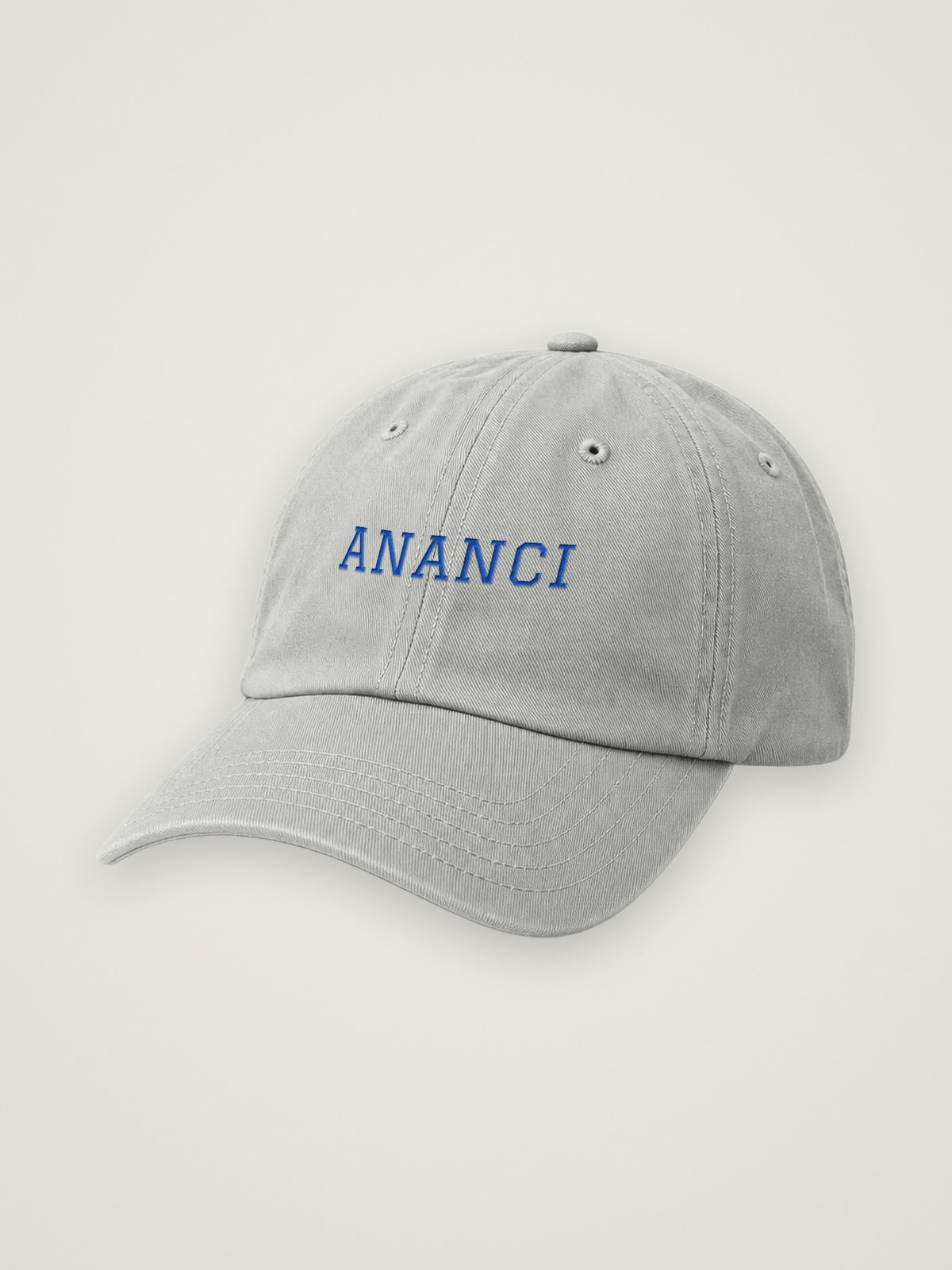 Heather Grey ANANCI dad hat with ANANCI embroidered in cobalt varsity lettering, on a warm stone background