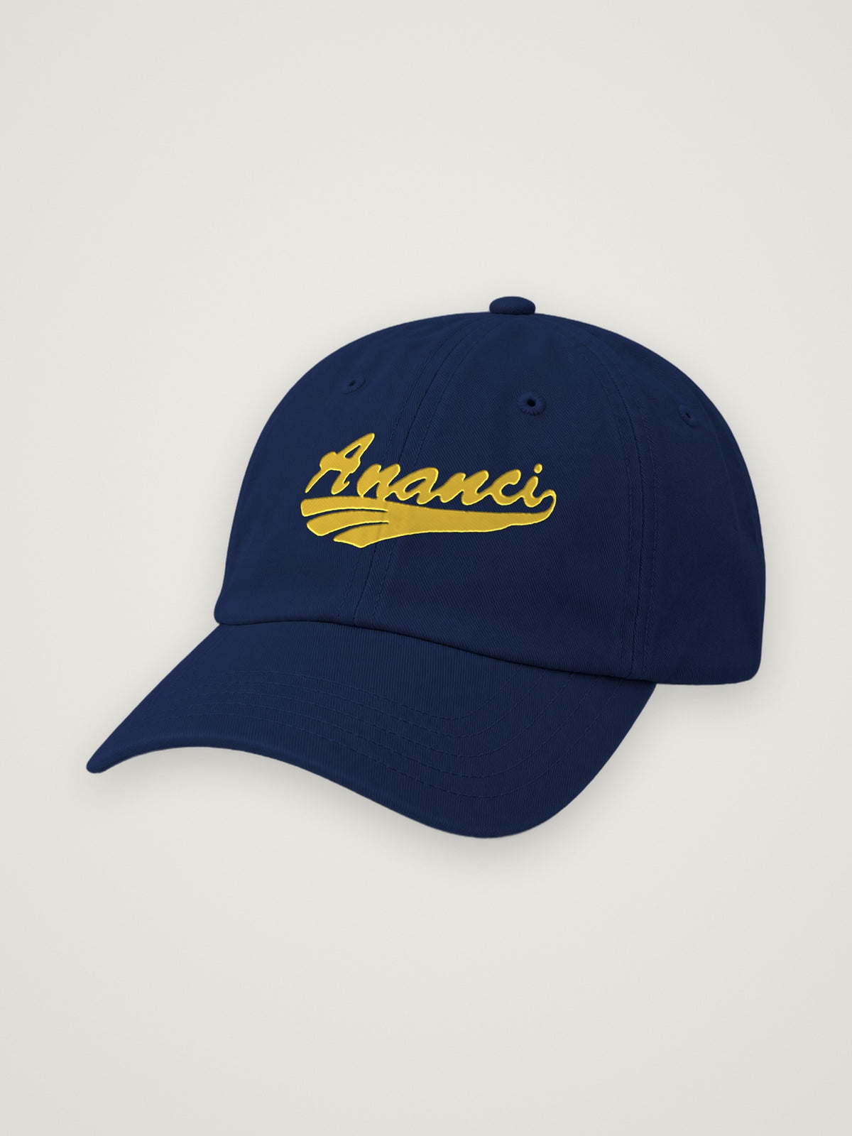 Navy ANANCI script dad hat with the wordmark embroidered in gold, on a warm stone background